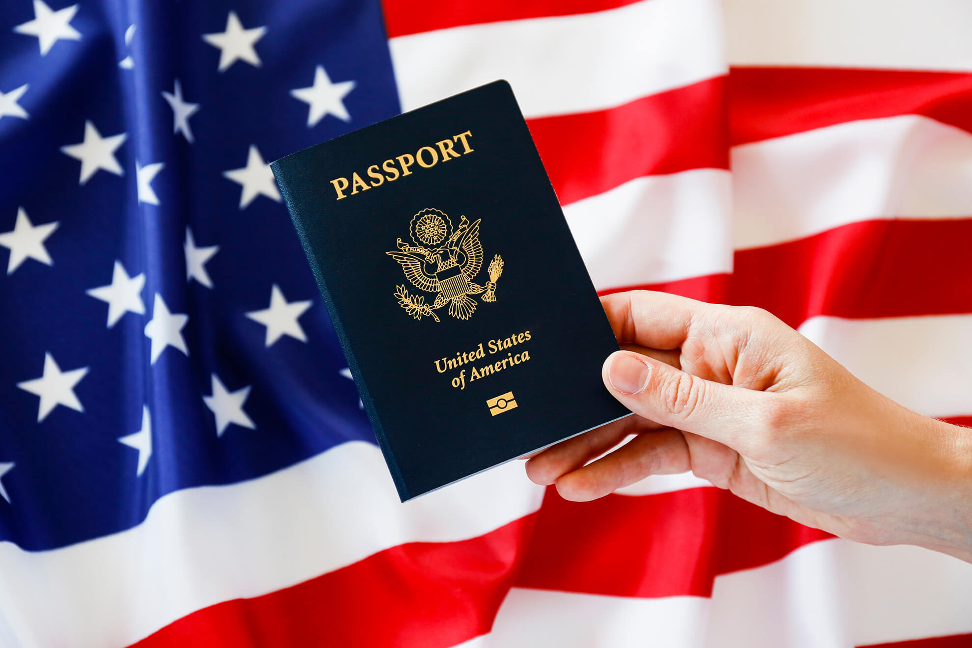 Man holding US Passport in front of United States Flag
